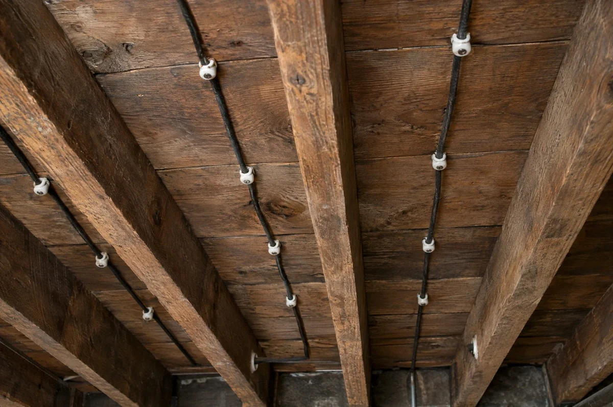 Illustration of older knob-and-tube wiring supported on porcelain insulators beneath exposed wood joists.