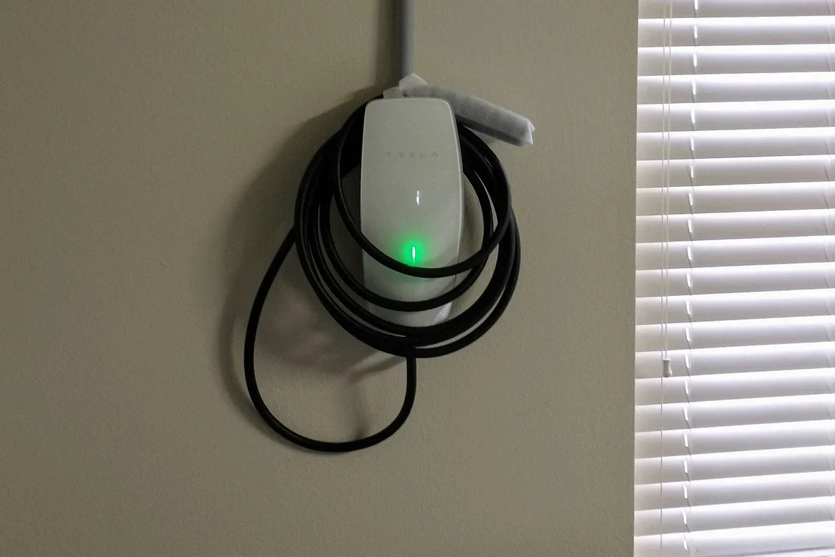 Reference photo of a Tesla Wall Connector installed on a garage wall, with its cable wrapped around the unit.