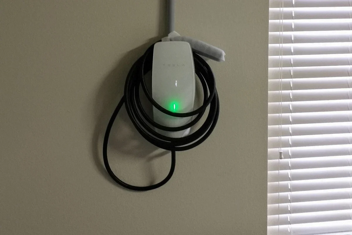Reference photo of a Tesla Wall Connector installed on a garage wall, with its cable wrapped around the unit.